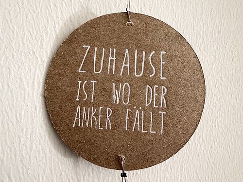 Rundes Wandschild mit der Aufschrift „Zuhause ist wo der Anker fällt“