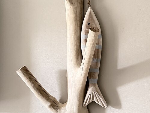 Gestreifter Holzfisch an einer Wandgarderobe aus einem hellen, verzweigten Ast