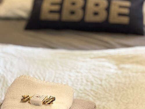 Gefaltete Handtücher mit einem verpackten Bonbon auf dem Einzelbett; dahinter ein Kissen mit der Aufschrift „Team Ebbe“