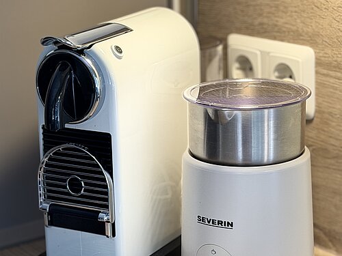 Weiße Kapselkaffeemaschine und elektrischer Milchaufschäumer auf der Küchenarbeitsplatte