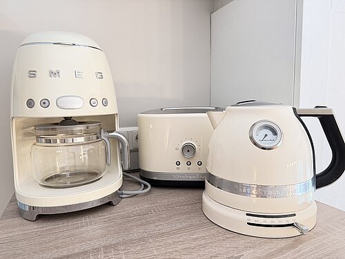 Cremefarbene Filterkaffeemaschine, Toaster und Wasserkocher auf einer hölzernen Küchenablage