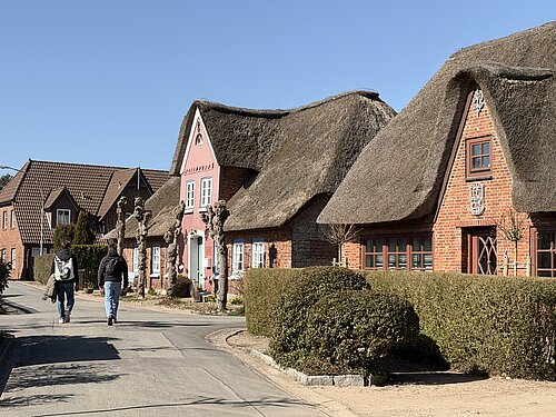 Straße in Wyk mit reetgedeckten Backsteinhäusern, geschnittenen Hecken und zwei Spaziergängern