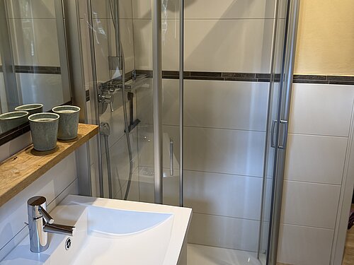 Gläserne Runddusche neben einem weißen Waschbecken mit verchromter Armatur und Spiegel