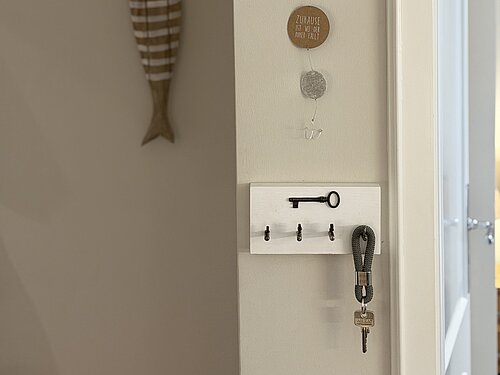 Garderobe mit gestreiftem Holzfisch, maritimer Hängedekoration und Schlüsselbrett neben der offenen Tür